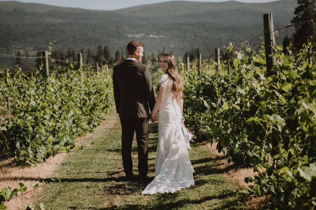 Couple walking through a vineyard in Kelowna in their wedding attire