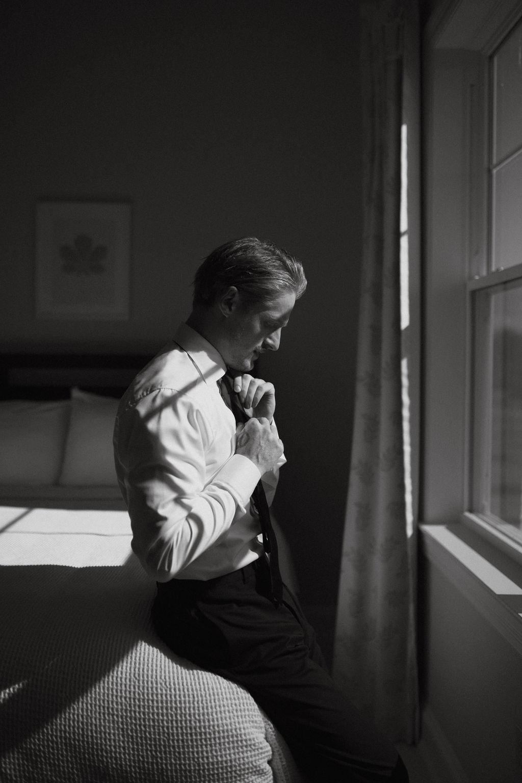 A groom puts on his tie before his wedding day, Fox Harb'r, NS