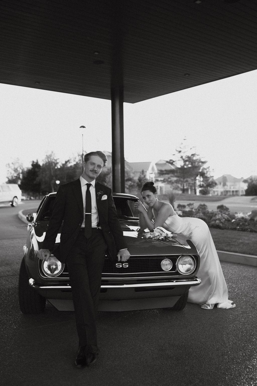 Bride and groom pose against classic car, Fox Harb'r, NS