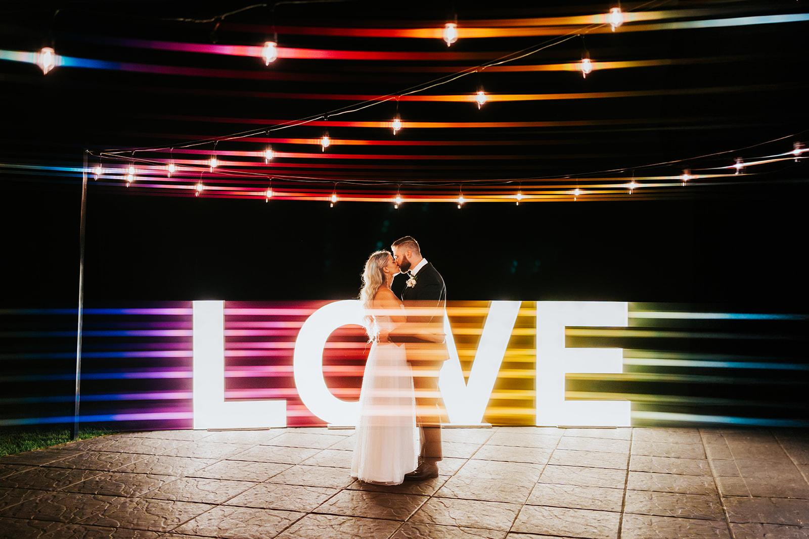 Bride and groom photographed in front of light up "love" sign with coloured light painting techniques