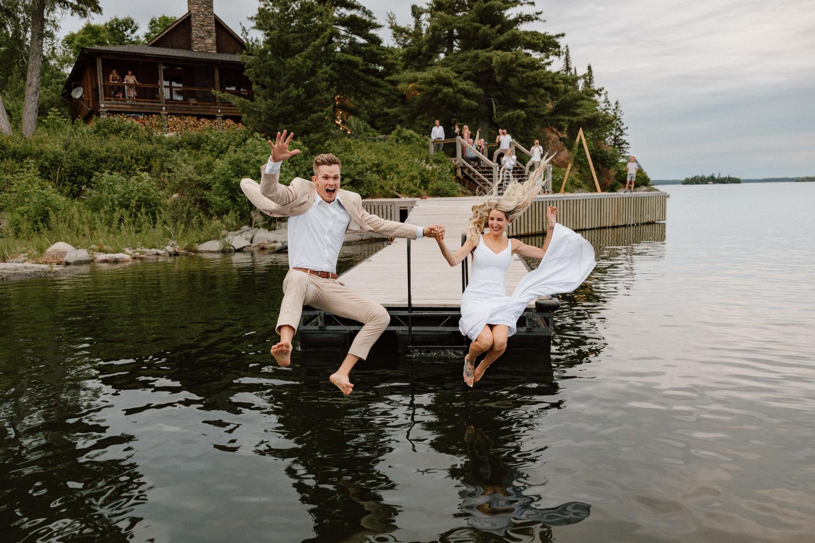 Bride and groom jump off a dock into a lake on their wedding day