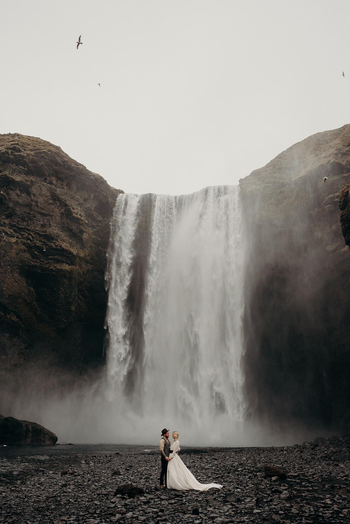 Wedding elopement in Iceland, bride and groom in front of the world famous Skógafoss waterfall.